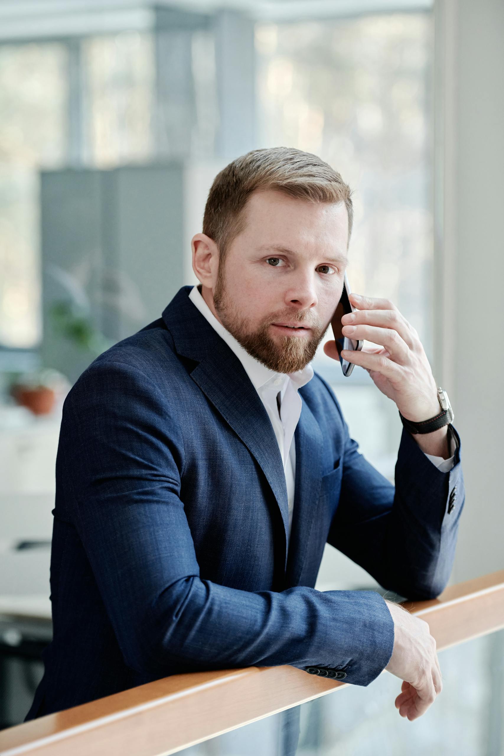 Businessman in blue suit talking on phone indoors, portraying professionalism and formal attire.