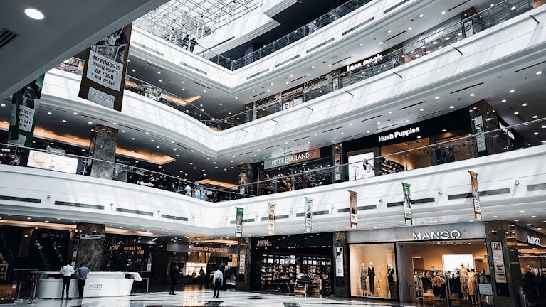 Spacious indoor view of a multi-story shopping mall with various branded stores and escalators.