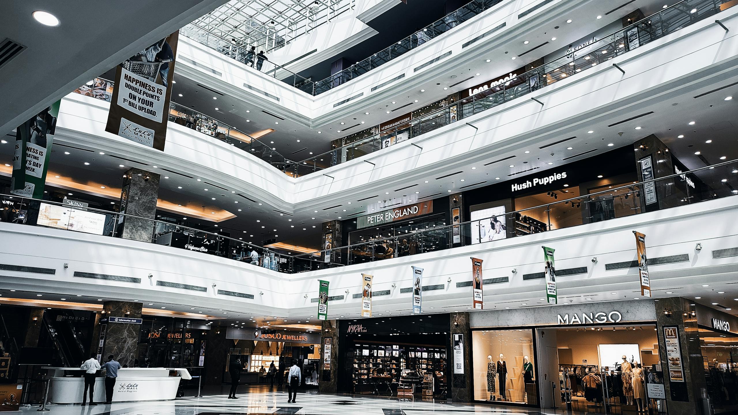 Spacious indoor view of a multi-story shopping mall with various branded stores and escalators.