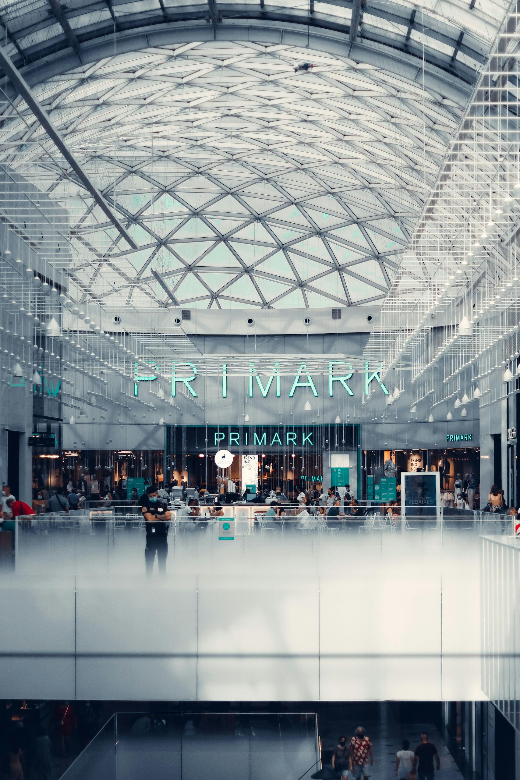 Spacious shopping mall interior featuring glass walls and Primark storefront.