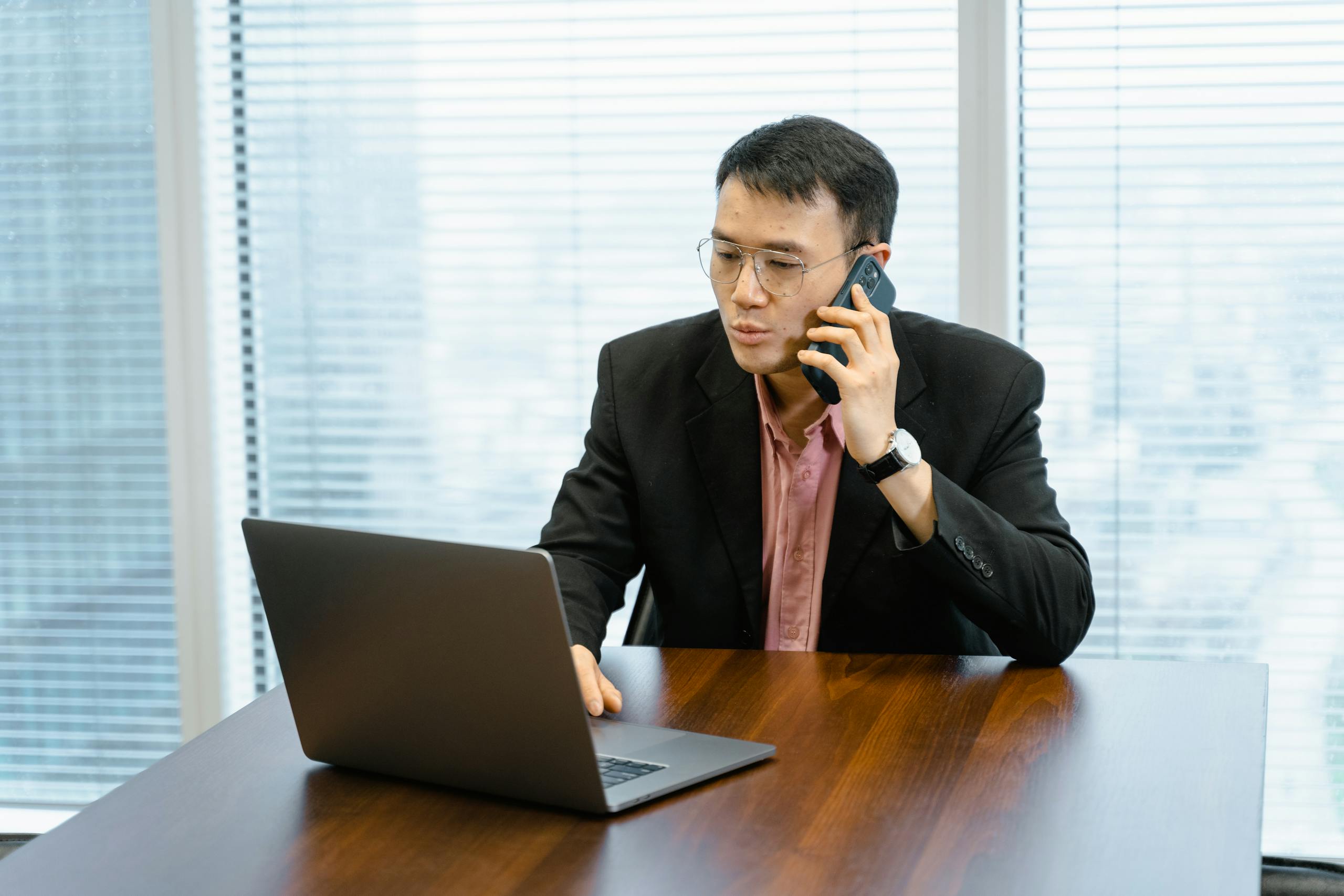 Businessman working remotely, talking on phone with laptop in office.